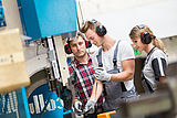 Junge Menschen in Arbeitskleidung mit Gehörschutz an einer Maschine