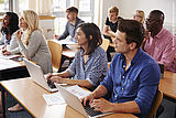 Acht Teilnehmende unterschiedlichen Alters und Geschlechts sitzen in einem Seminar, teils mit aufgeklappten Laptops vor sich oder beim Schreiben auf einen Block.