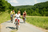 Eine dreiköpfige Familie fährt bei warmem Wetter mit dem Fahrrad durch die Natur. (Quelle: AdobeStock: Kzenon)