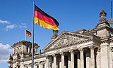 Vor und auf dem deutschen Reichstagsgebäude in Berlin wehen zwei Deutschlandfahnen im Wind.
