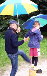 Mann assistiert einem balancierenden Mädchen. Beide tragen einen Regenschirm © Foto: Sylvia Krell